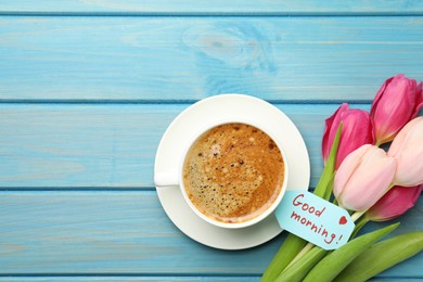 Photo of Cup of aromatic coffee, beautiful pink tulips and Good Morning note on light blue wooden table, flat lay. Space for text