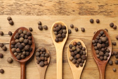 Aromatic allspice pepper grains in spoons on wooden table, flat lay