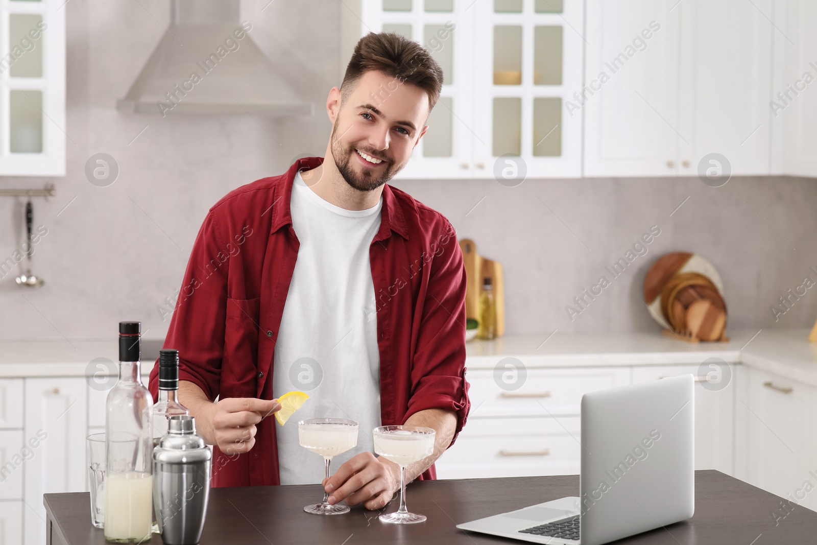 Photo of Happy man decorating cocktail with lemon at table in kitchen. Time for hobby