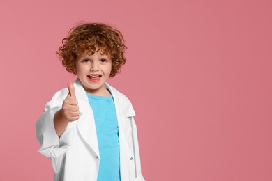 Little boy in medical uniform showing thumb up on pink background. Space for text