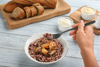 Photo of Woman eating delicious brown rice at white wooden table, closeup