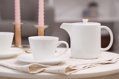 Cups of tea, teapot and candles on white table, closeup