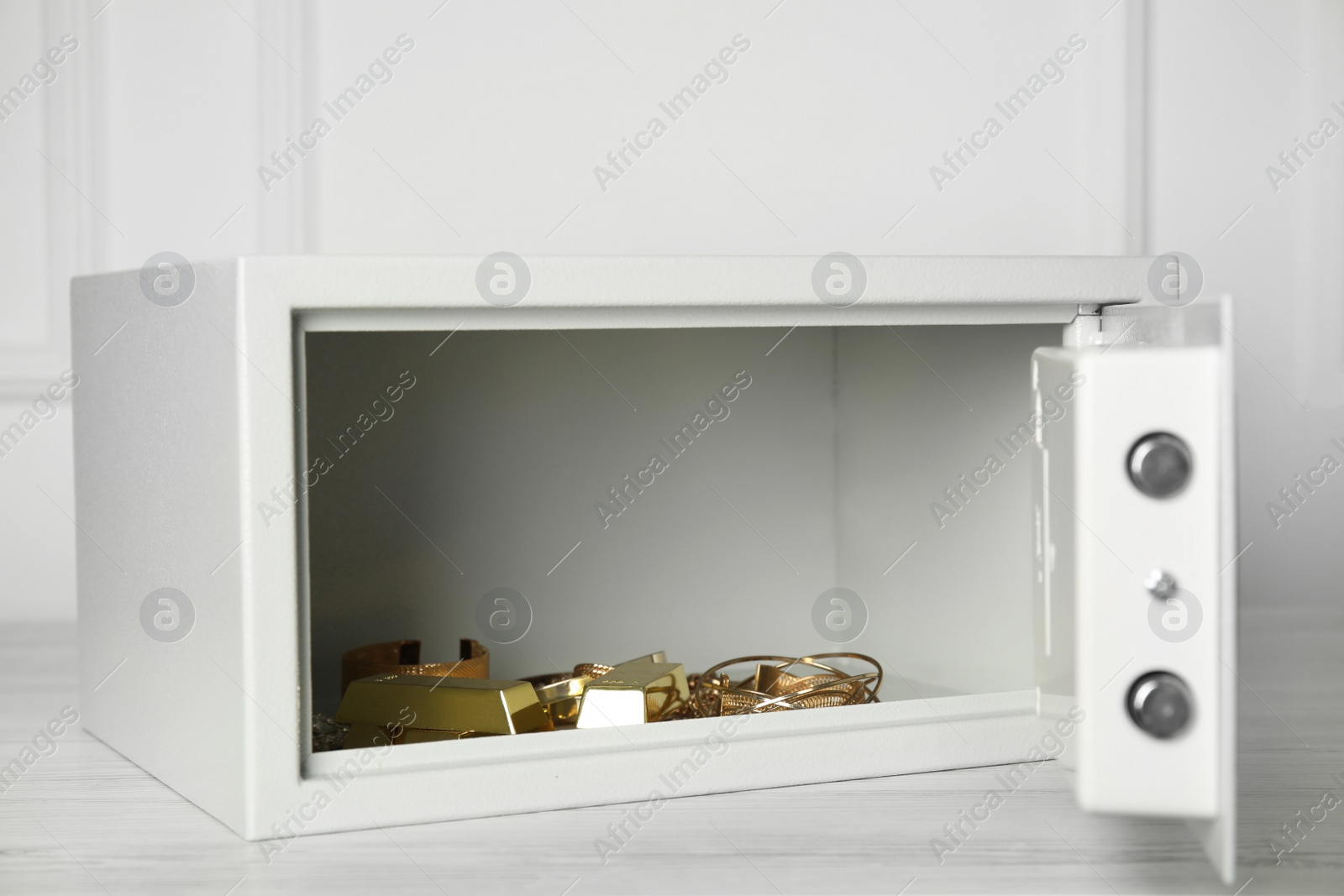 Photo of Open steel safe with gold bars and jewelry on wooden table