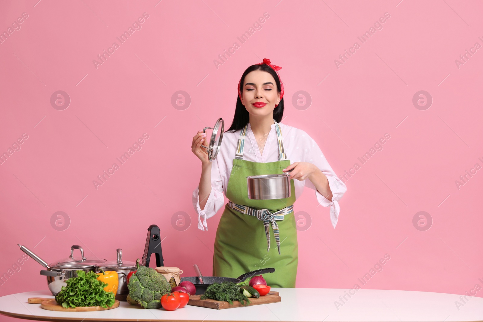 Photo of Young housewife with vegetables and different utensils on pink background