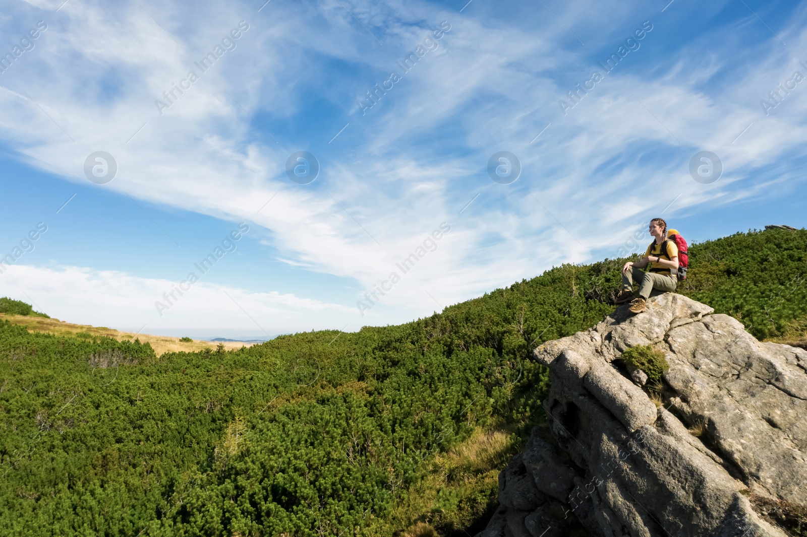 Image of Young woman with backpack on rocky cliff in mountains