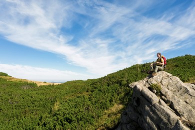 Image of Young woman with backpack on rocky cliff in mountains