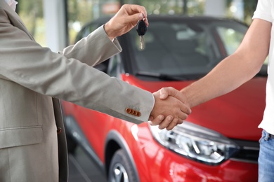 Salesman shaking hands with customer while giving car key in auto dealership, closeup