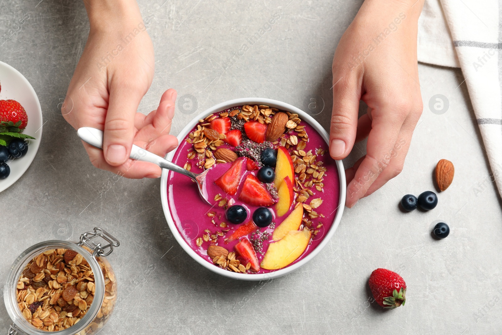 Photo of Woman eating delicious acai smoothie at grey table, top view