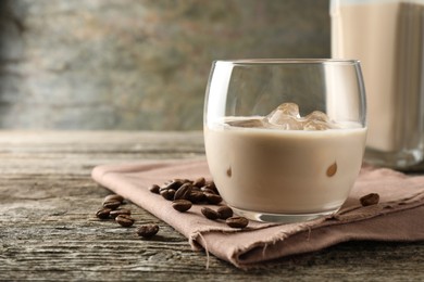 Coffee cream liqueur in glass and beans on wooden table, closeup