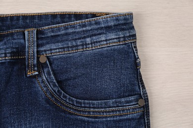 Stylish blue jeans on wooden background, closeup of inset pocket