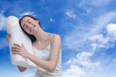 Happy woman with orthopedic pillow against blue sky, space for text