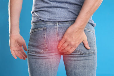 Image of Man suffering from hemorrhoid on light blue background, closeup