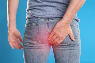 Man suffering from hemorrhoid on light blue background, closeup