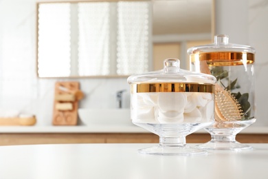 Jars with cotton pads and hairbrush on table in bathroom