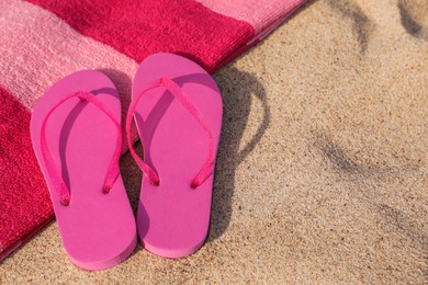 Beach towel and slippers on sand, space for text