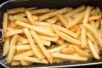 Cooking delicious french fries in hot oil, closeup