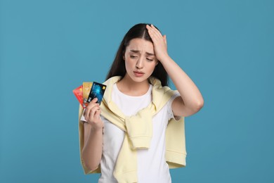 Photo of Worried woman with credit cards on light blue background. Debt problem