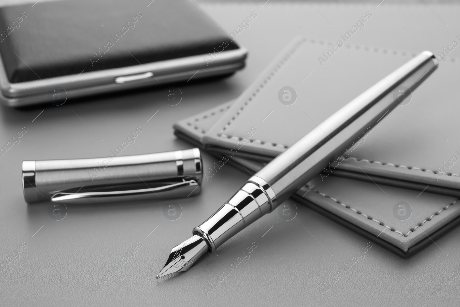 Photo of Stylish silver fountain pen and cigarette case on grey textured table, closeup