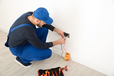 Photo of Electrician with tester checking voltage indoors, space for text