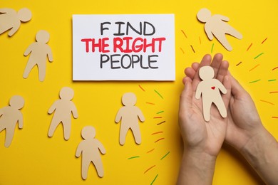 Photo of Find the right people. Woman choosing human paper figure with drawn heart among others without it on yellow background, top view