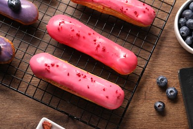 Photo of Tasty glazed eclairs and blueberries on wooden table, flat lay