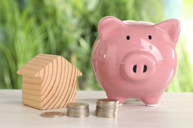 Wooden house model, stacked coins and piggy bank on light table outdoors