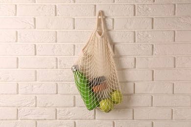 Photo of Net bag with different items hanging on brick wall. Conscious consumption
