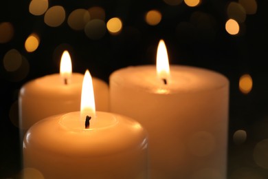 Wax candles burning on black background with blurred lights, closeup. Bokeh effect