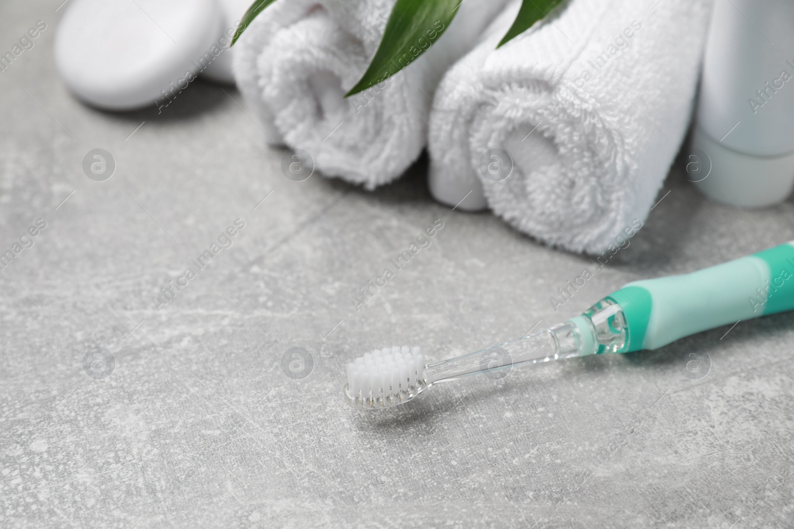 Photo of Electric toothbrush, tube of paste and rolled towels on grey textured table, closeup