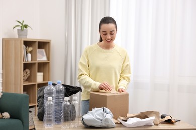 Smiling woman with cardboard box separating garbage in room