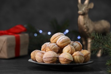 Photo of Plate of tasty nut shaped cookies with powdered sugar on black table. Space for text