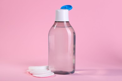 Photo of Open bottle of micellar water and cotton pads on pink background