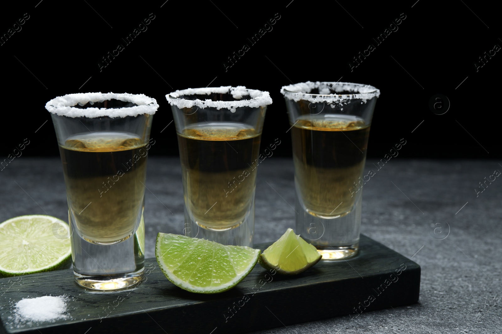 Photo of Mexican Tequila shots, lime slices and salt on grey table