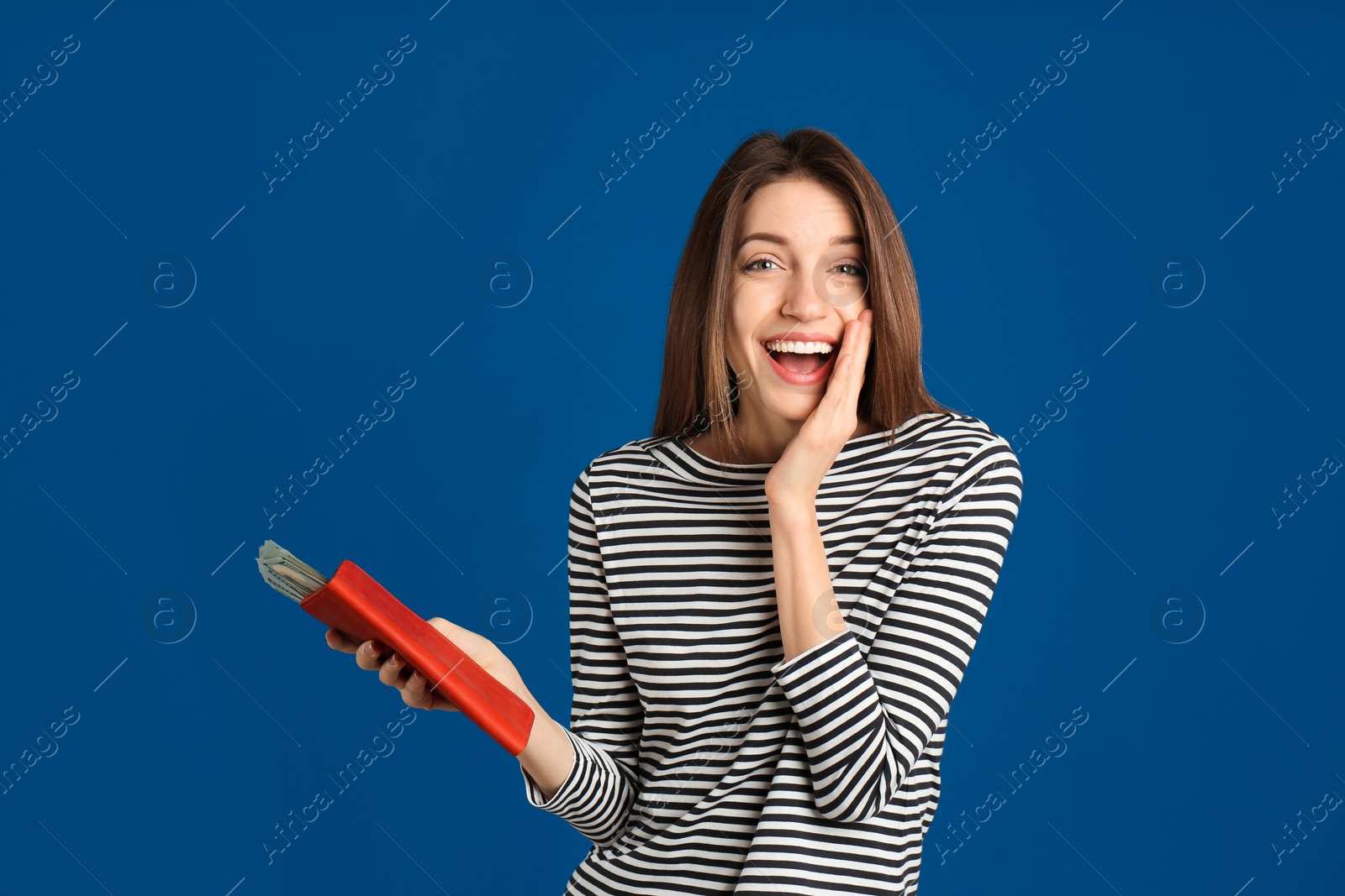 Photo of Happy young woman holding wallet with money on blue background