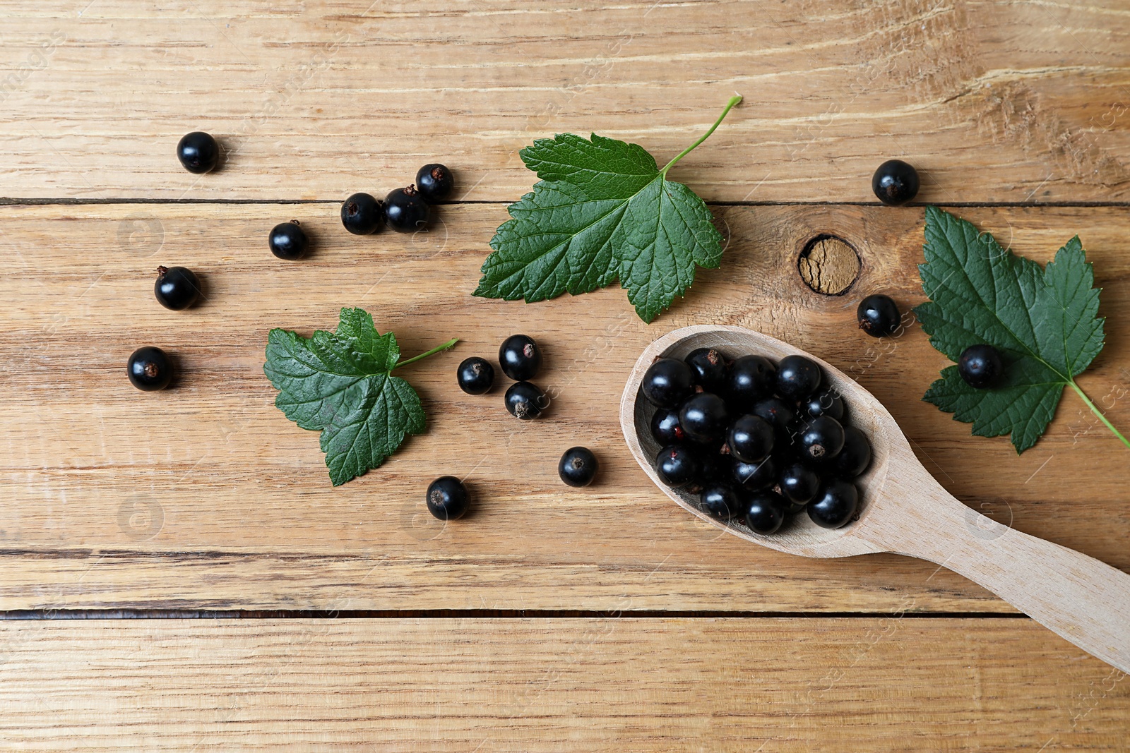 Photo of Ripe blackcurrants and leaves on wooden table, flat lay