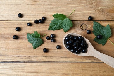 Photo of Ripe blackcurrants and leaves on wooden table, flat lay