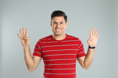 Photo of Man showing number eight with his hands on grey background