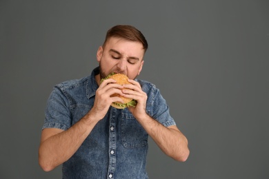 Photo of Young man eating tasty burger on grey background. Space for text