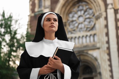 Photo of Young nun with Bible near cathedral outdoors. Space for text