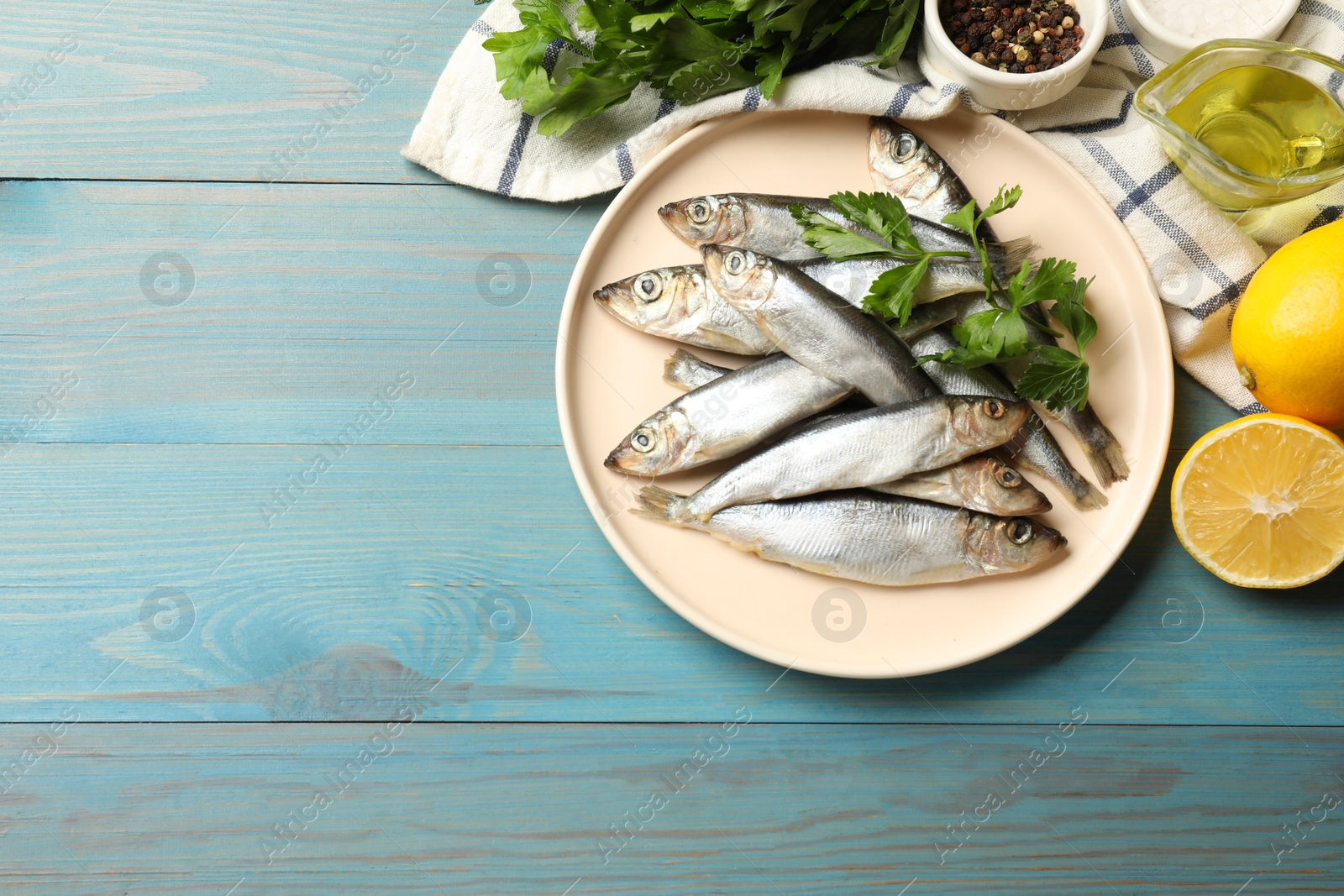 Photo of Fresh raw sprats, parsley and other products on light blue wooden table, flat lay. Space for text