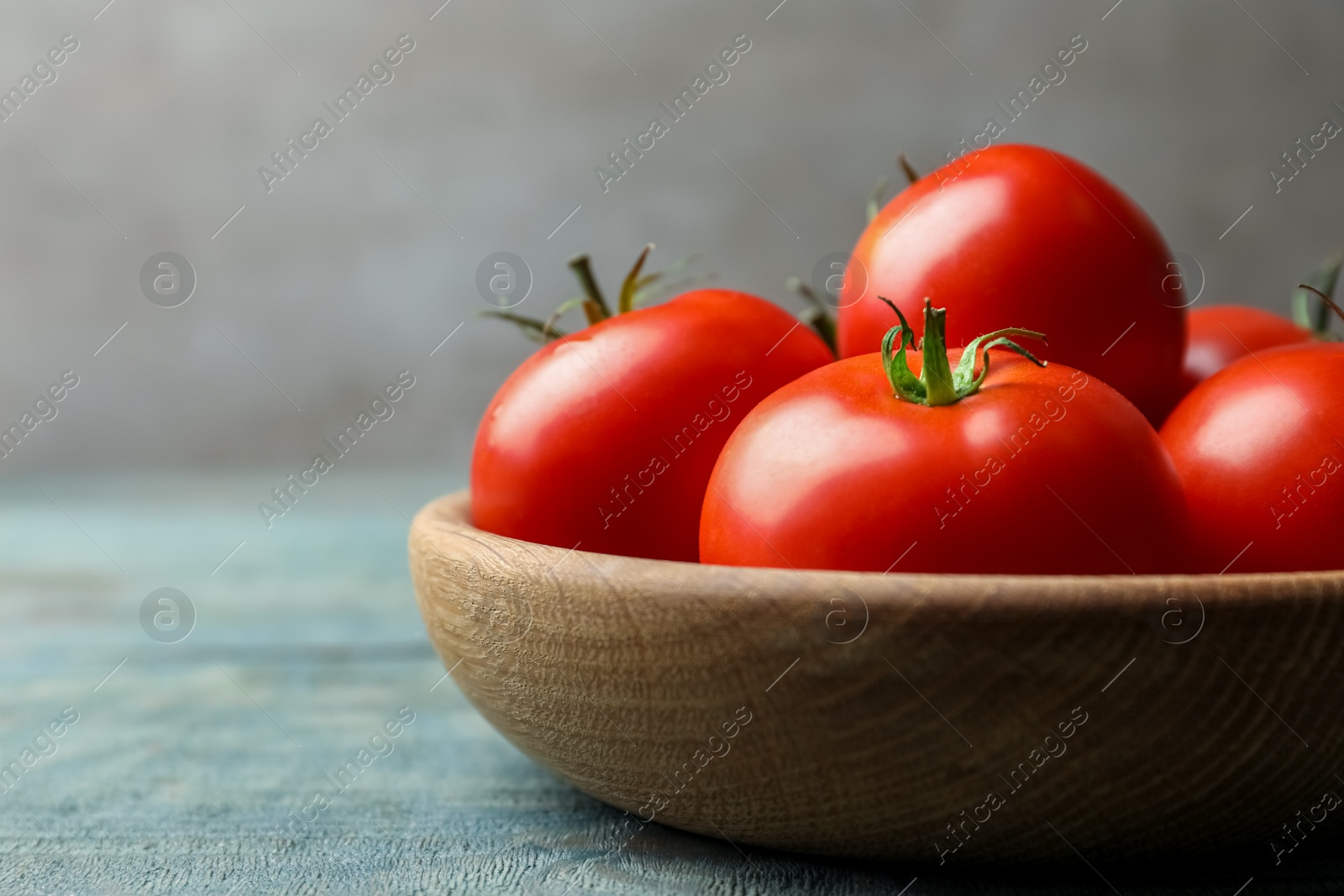 Photo of Ripe tomatoes in bowl on blue wooden table, closeup. Space for text