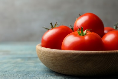 Photo of Ripe tomatoes in bowl on blue wooden table, closeup. Space for text