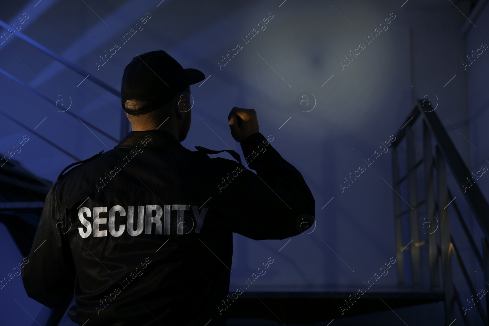 Photo of Male security guard with flashlight on stairs in darkness