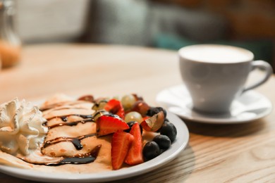 Photo of Delicious pancake with fresh fruits and cup of aromatic coffee on wooden table, closeup