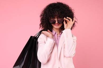 Photo of Happy young woman with shopping bags and stylish sunglasses on pink background