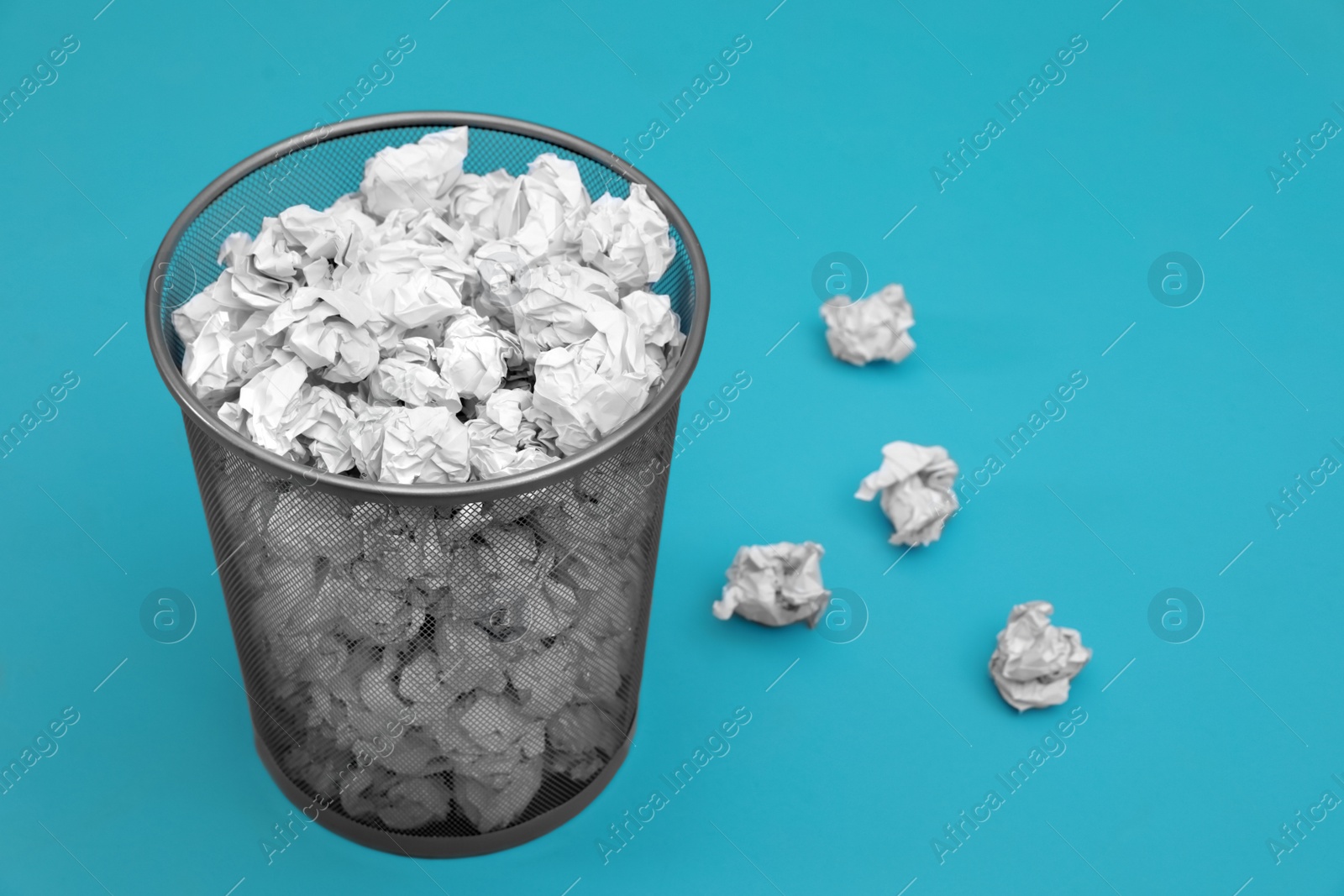 Photo of Metal bin with crumpled paper on color background, space for text