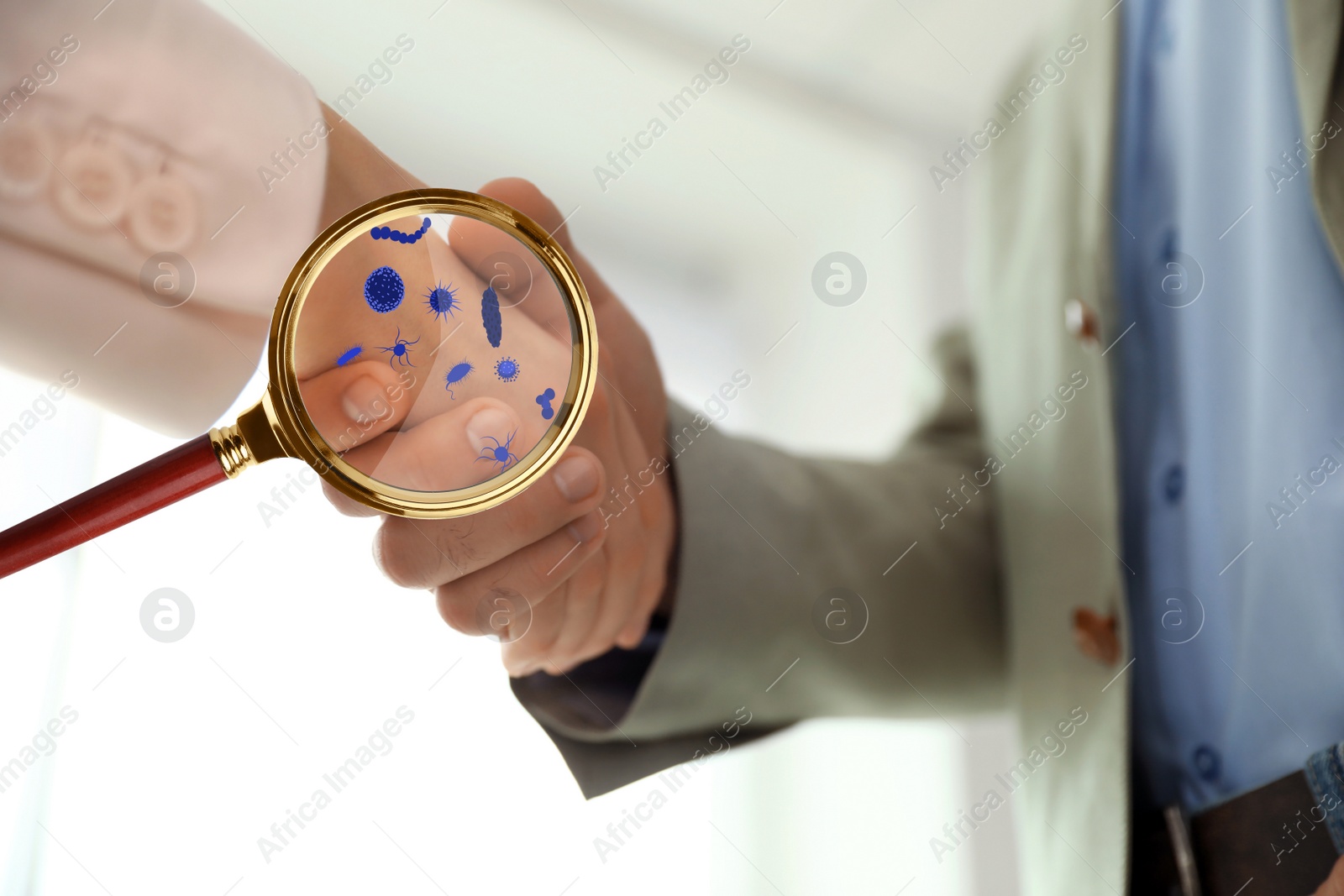 Image of Magnifying glass detecting microbes and business partners shaking hands, closeup