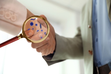 Image of Magnifying glass detecting microbes and business partners shaking hands, closeup