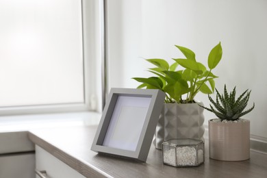 Beautiful Scindapsus and Aloe in pots with blank photo frame on wooden table, space for text. Different house plants