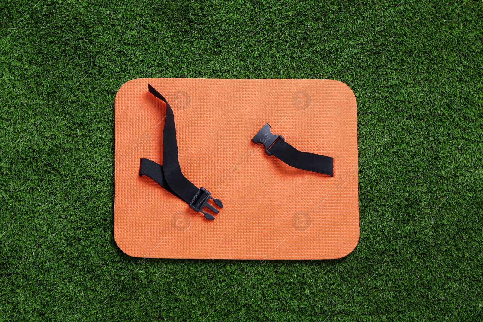 Photo of Orange foam seat mat for tourist on green grass, top view